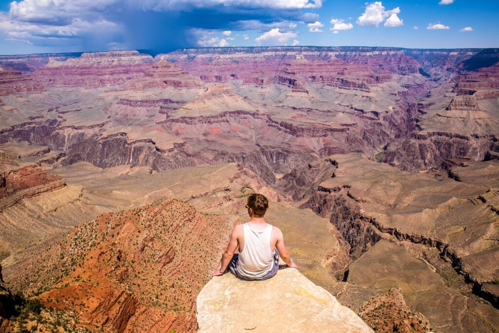 a man sitting on edge of a cliff at the Grand Canyon